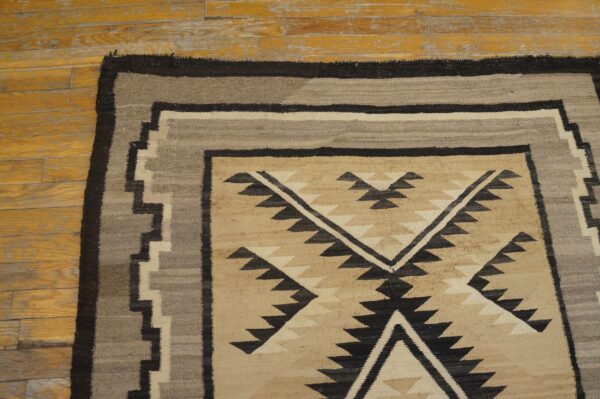 Tan, gray, and black geometric flatweave rug detail on a distressed yellow wood floor.