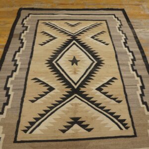 Tan and black geometric rug with a central diamond design, bordered by gray, lies on distressed wooden flooring.