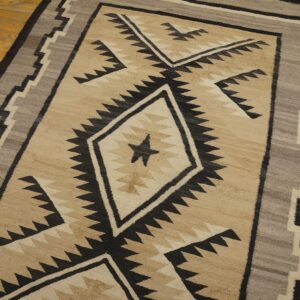 Beige, black, and gray geometric flatweave rug with sawtooth borders and a central star on wood flooring.