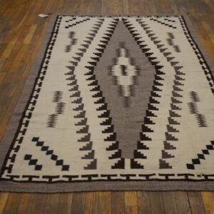 A cream, gray, and brown flatweave rug with a geometric pattern lies on a distressed hardwood floor.