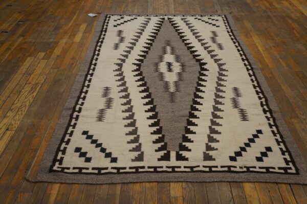 A cream, gray, and brown flatweave rug with a geometric pattern lies on a distressed hardwood floor.