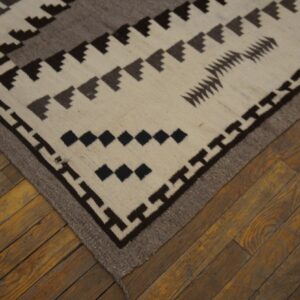 Cream, brown, and gray flatweave rug featuring stepped geometric patterns on rustic wood floors.