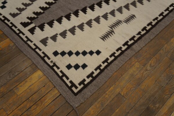 Cream, brown, and gray flatweave rug featuring stepped geometric patterns on rustic wood floors.