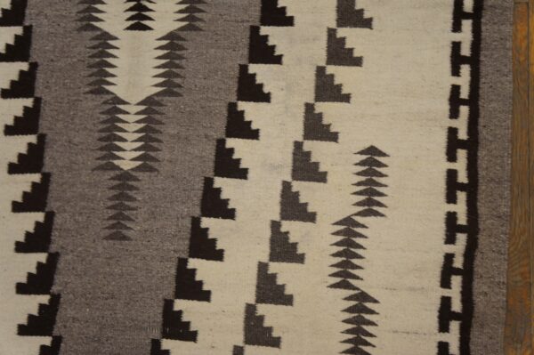 Flatwoven rug detail with black, gray, and cream geometric patterns shown next to a wood edge.
