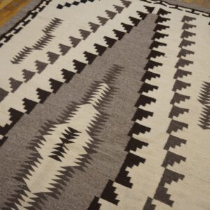 Cream flat-weave rug featuring bold brown and gray geometric stepped patterns on hardwood flooring.