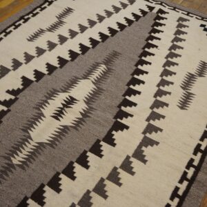 Cream, gray, and brown flat-weave rug with a Southwestern style geometric design over hardwood flooring.