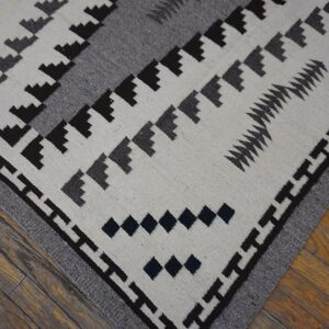 Close-up of a white and gray flatweave rug with dark geometric motifs resting on hardwood flooring.