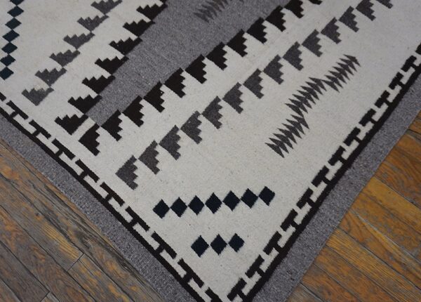 Close-up of a white and gray flatweave rug with dark geometric motifs resting on hardwood flooring.