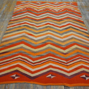 Flatweave rug featuring orange, maroon, gray, and yellow zigzag stripes on distressed wood planks.