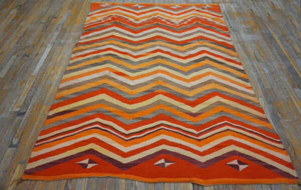 Flatweave rug featuring orange, maroon, gray, and yellow zigzag stripes on distressed wood planks.