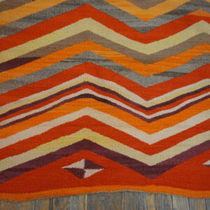 Flatweave rug with thick orange, gray, burgundy, and cream chevron stripes on weathered wood planks.