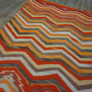 Low-pile rug with geometric orange, brown, and cream chevron stripes on weathered gray wood flooring.