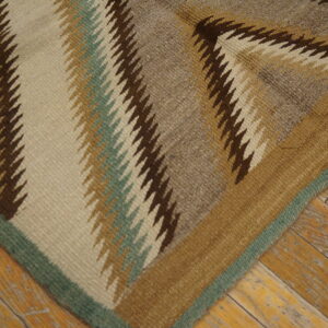 Flatweave rug corner with zigzag patterns in neutral and sage colors against worn wood planks.