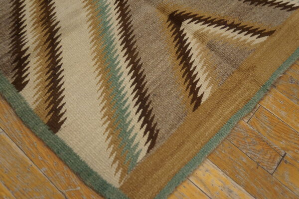 Flatweave rug corner with zigzag patterns in neutral and sage colors against worn wood planks.
