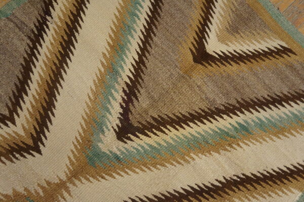 Flatweave rug with serrated zigzag patterns in beige, dark brown, tan, and muted teal.