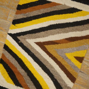 Flatwoven rug featuring angular stripes of yellow, black, white, brown, and grey on wood floor.