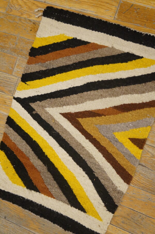 Flatwoven rug featuring angular stripes of yellow, black, white, brown, and grey on wood floor.