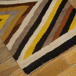 Flatweave rug with zigzag stripes in yellow, black, brown, and gray on distressed wood flooring.