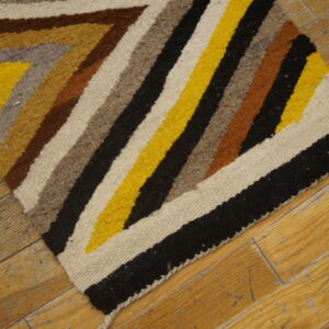 Low-pile rug with yellow, black, brown, and cream zig-zag pattern displayed on textured wooden planks.