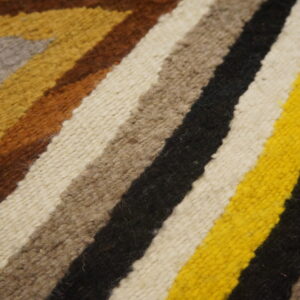 Close-up of a woven rug with wide geometric stripes in bright yellow, black, white, brown, and gray.