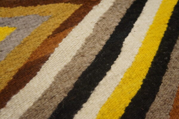 Close-up of a woven rug with wide geometric stripes in bright yellow, black, white, brown, and gray.