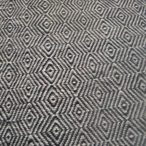 Black and cream woven rug featuring a repeating geometric diamond pattern resting on wood flooring.