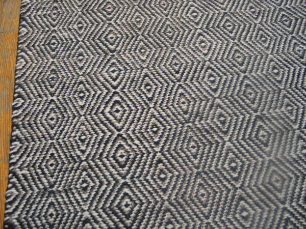 Black and cream woven rug featuring a repeating geometric diamond pattern resting on wood flooring.