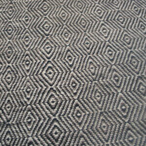 Flatweave rug with a repeating black, gray, and white geometric diamond pattern shown against wood flooring.