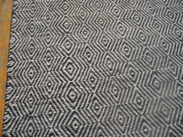 Flatweave rug with a repeating black, gray, and white geometric diamond pattern shown against wood flooring.