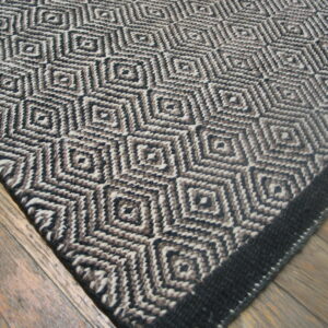 Textured rug with interlocking diamonds in black, brown, and off-white rests on rustic wood flooring.