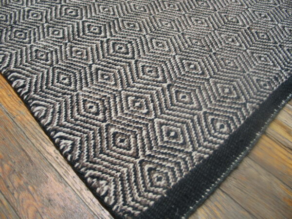 Textured rug with interlocking diamonds in black, brown, and off-white rests on rustic wood flooring.