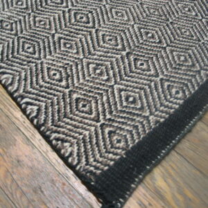 A flat-woven rug featuring a diamond pattern in black, beige, and brown on wood flooring.