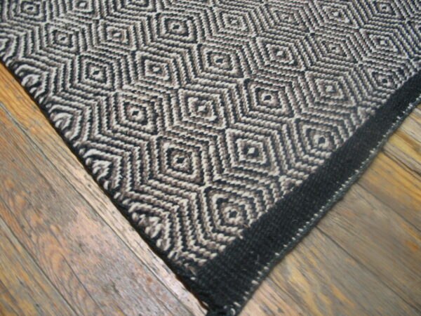 A flat-woven rug featuring a diamond pattern in black, beige, and brown on wood flooring.