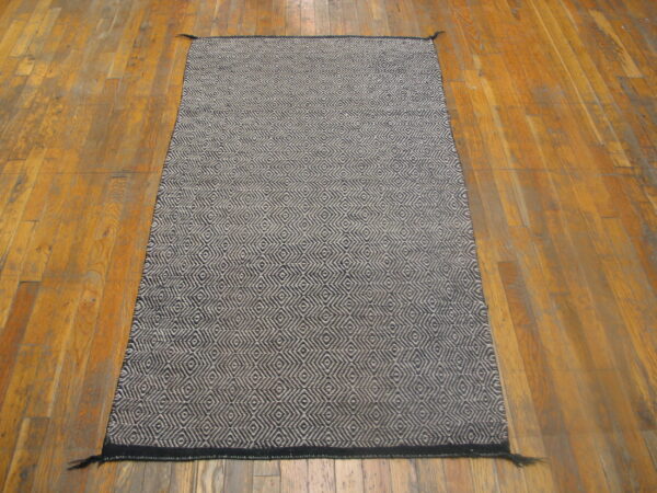 Dark blue and beige woven runner rug with a dense geometric pattern on distressed wood flooring.