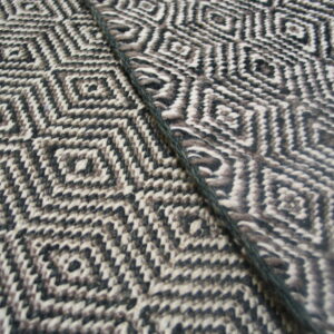 Detailed view of a woven rug showing black, white, and gray geometric diamonds alongside a dark cord.