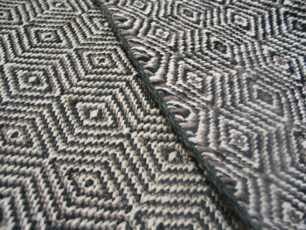 Detailed view of a woven rug showing black, white, and gray geometric diamonds alongside a dark cord.