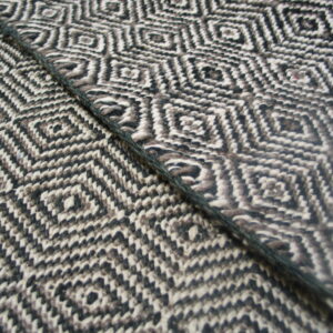 Black, white, and brown textured rug featuring a geometric diamond pattern and a dark diagonal cord.