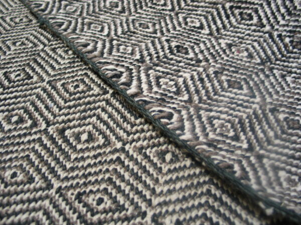 Black, white, and brown textured rug featuring a geometric diamond pattern and a dark diagonal cord.