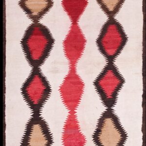 Narrow flatweave rug featuring three columns of serrated red, tan, and dark brown diamonds on a cream field over wood flooring.