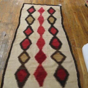 Flatwoven rug runner featuring serrated red, tan, and brown geometric diamond motifs on light wood flooring.