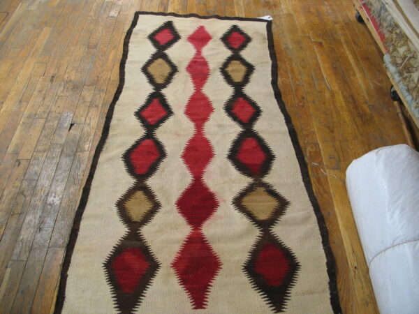 Flatwoven rug runner featuring serrated red, tan, and brown geometric diamond motifs on light wood flooring.