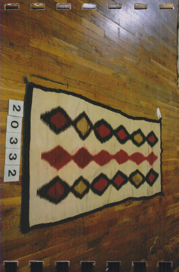 Cream rug with black borders and rows of serrated red and tan diamonds on hardwood floor.