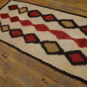 Cream, red, tan, and dark brown rug with zig-zag diamond motifs displayed on natural wood flooring.