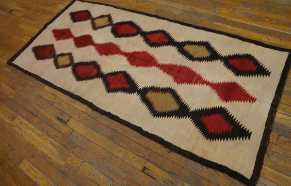 Cream, red, tan, and dark brown rug with zig-zag diamond motifs displayed on natural wood flooring.