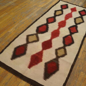 Cream runner rug featuring geometric serrated diamonds in red, khaki, and dark brown on hardwood flooring.