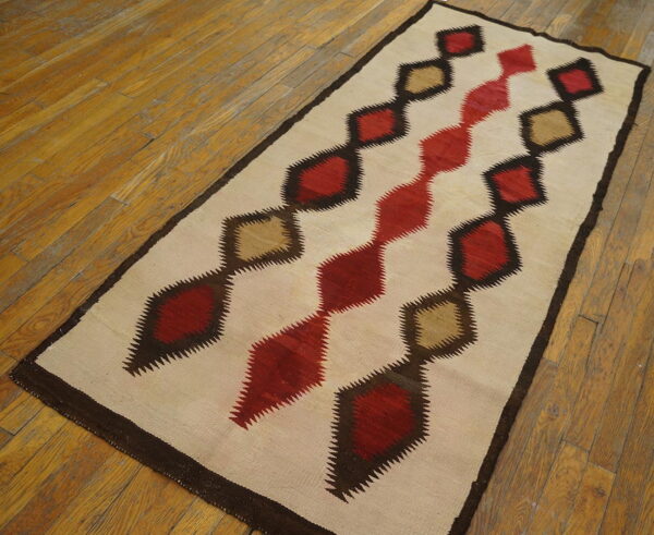 Cream runner rug featuring geometric serrated diamonds in red, khaki, and dark brown on hardwood flooring.