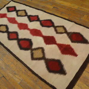 Flatwoven rug with cream ground and jagged red, brown, and tan diamonds rests on wooden plank flooring.