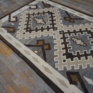 Geometric gray, brown, and cream flatweave rug displayed on weathered gray wood flooring.