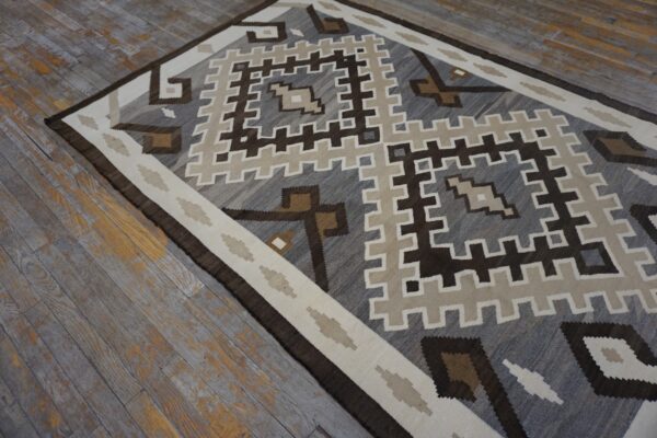 Geometric gray, brown, and cream flatweave rug displayed on weathered gray wood flooring.