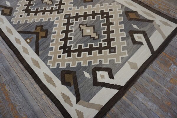 Flat-weave rug with geometric brown, gray, and cream stepped patterns on distressed wood flooring.